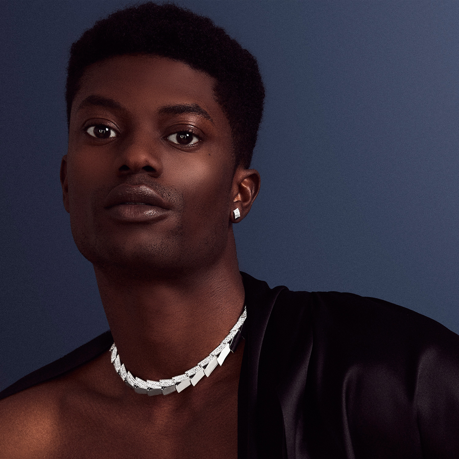 This is a photo of a male model wearing the Renisis Light Halo Necklace crafted in Platinum with pavé diamonds. He is photographic in dramatic lighting that reflects off the necklace.